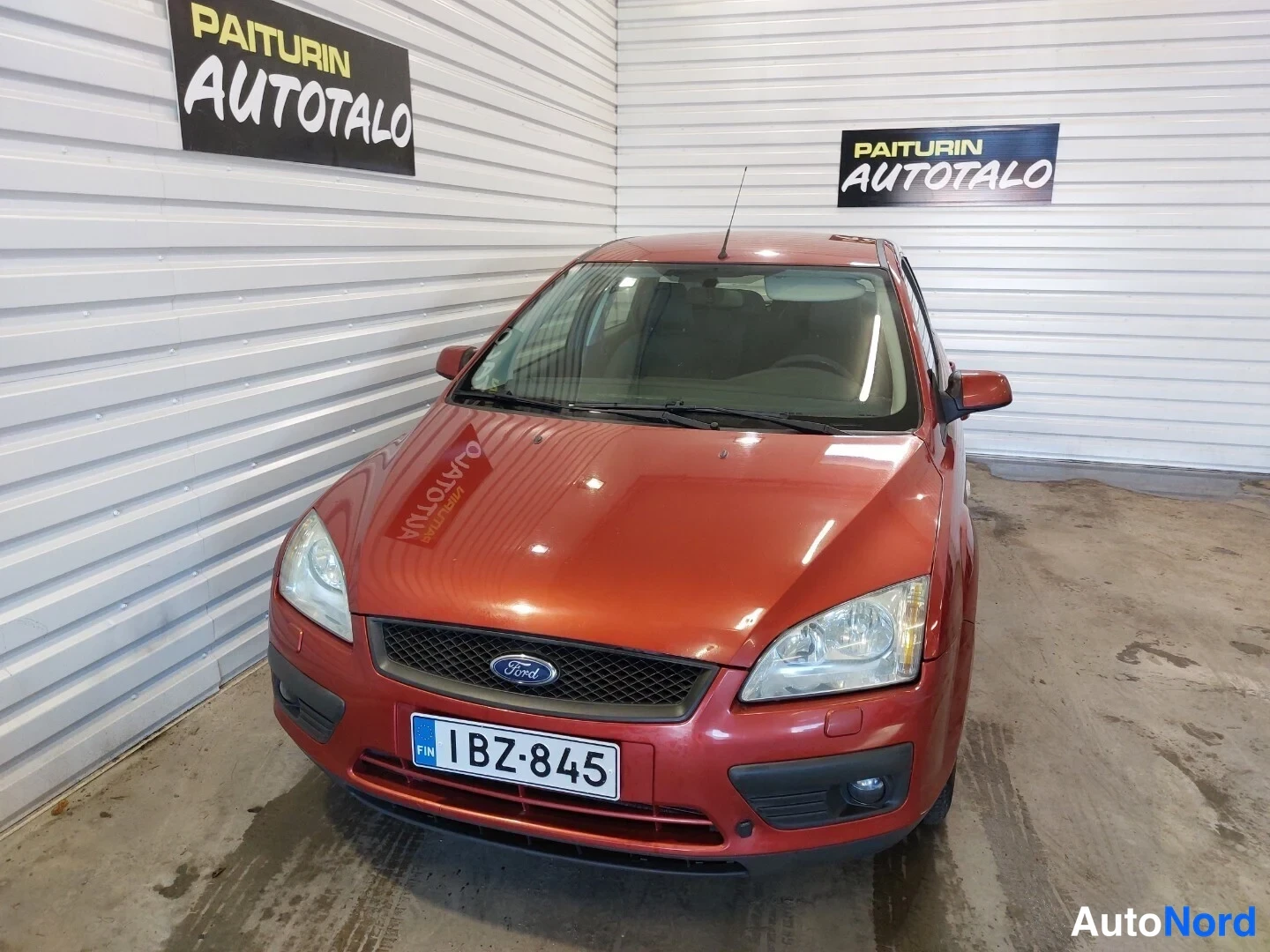 Edestä: Punaisen Ford-henkilöautin etupää kuvattuna autotallissa; etusäleikkö, ajovalot, sumuvalot ja rekisterikilpi näkyvissä.