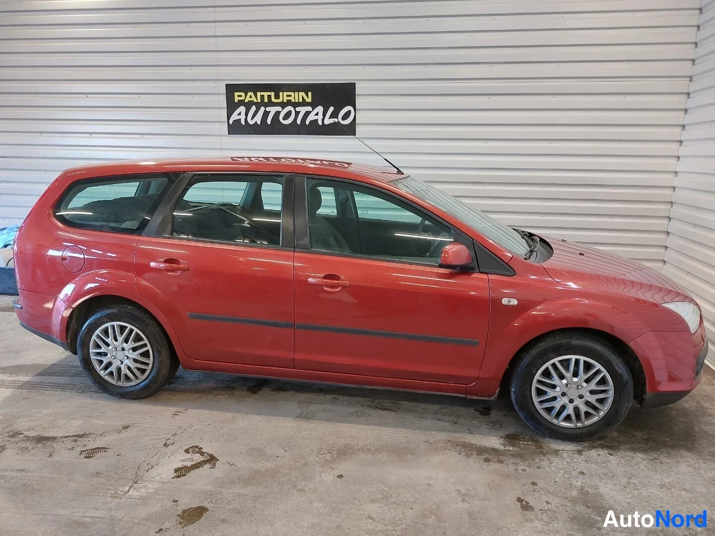 Etuviisto, nokka oikealle: Punaisen Ford Focus -farmarin sivukulma sisätiloissa; kylki ja keulan oikea reuna näkyvissä.