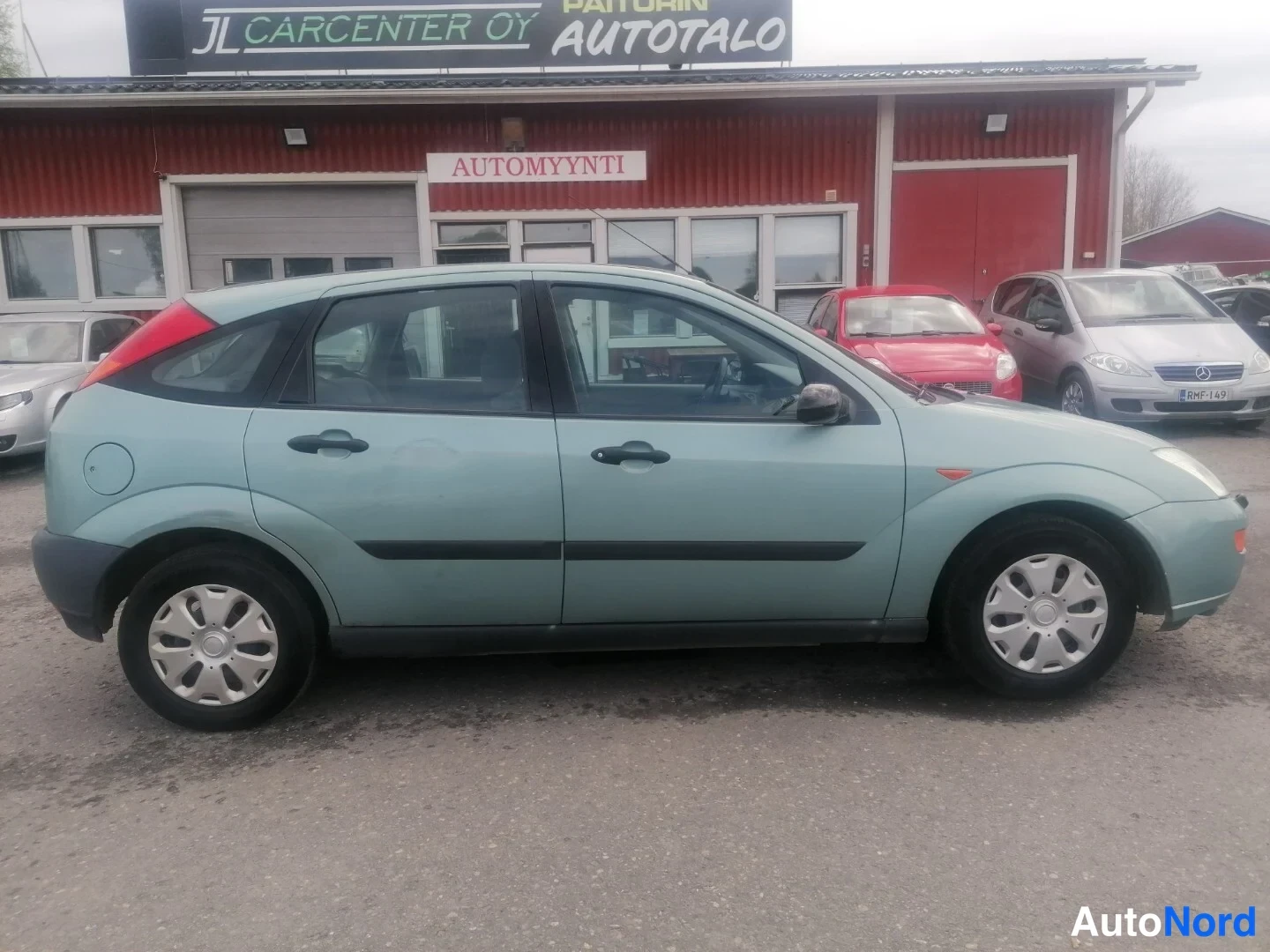 Sivulta: Sinivihreä Ford Focus sivusta vasemmalta autoliikkeen edessä.