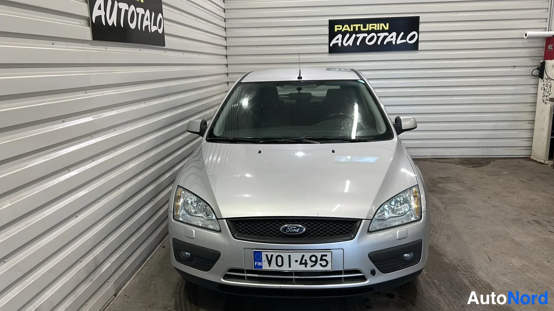 Edestä: Hopeanvärinen Ford Focus suoraan edestä kuvattuna sisätiloissa; Ford-merkki keulakorissa ja rekisterikilpi VO1-495 näkyvät.