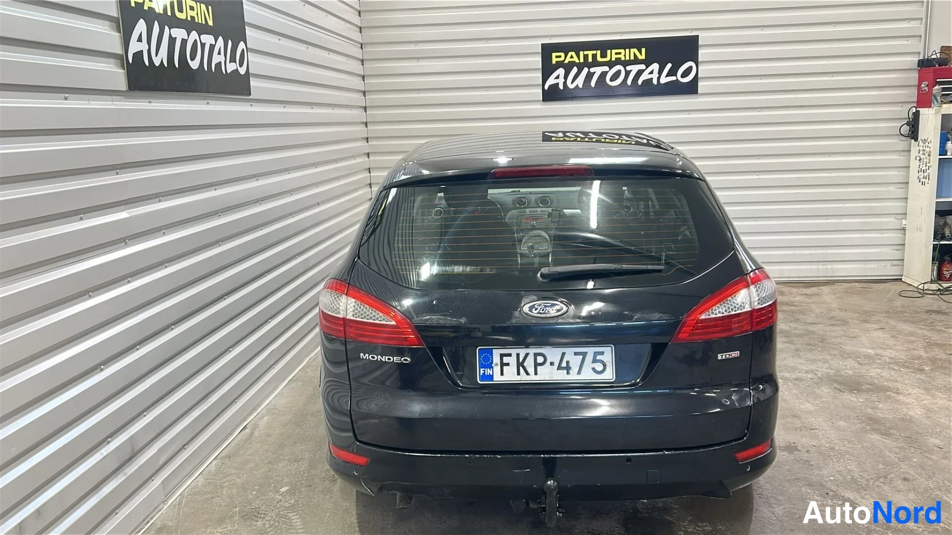 Takaa: Musta farmariauto suoraan takaa valokuvattuna hallissa, rekisterikilpi ja Mondeo-teksti näkyvät.