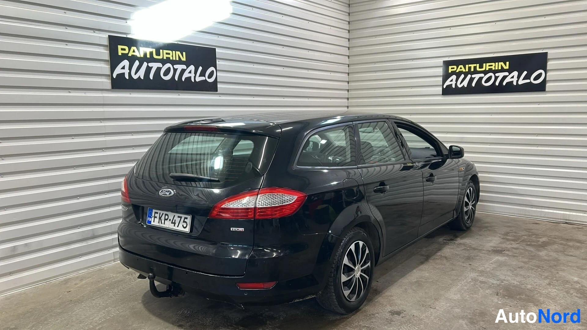 Takaviisto: Musta farmariauto takakulmasta hallissa, takaosa ja kylki näkyvät, rekisterikilpi.