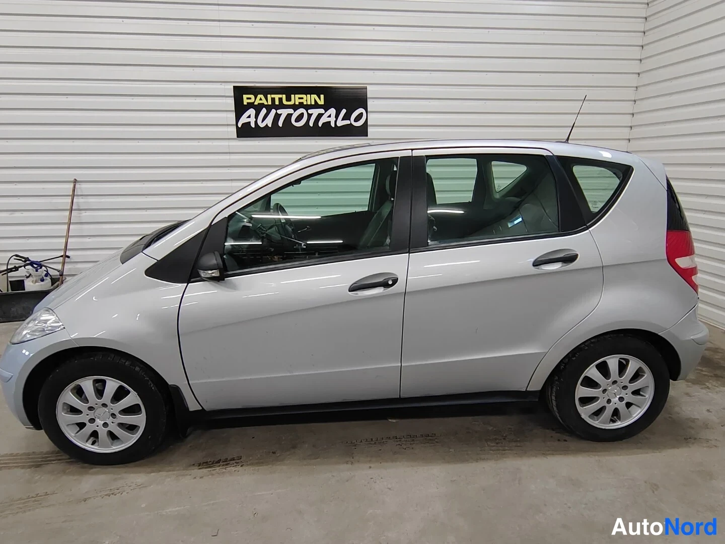 Sivulta: Profile view of a silver five-door hatchback parked indoors against a corrugated white wall.