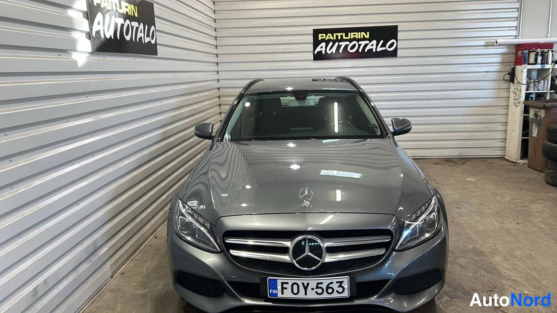 Edestä: Auton etupää suoraan edestä; harmaan metallinhohtoinen Mercedes, Mercedes-merkki grillissä, rekisteri.