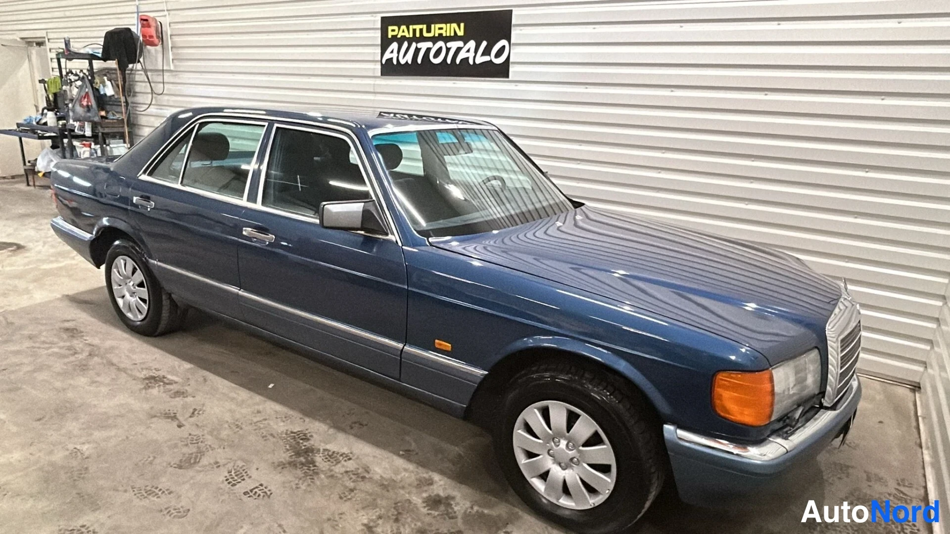 Etuviisto, nokka oikealle: Sininen Mercedes-SEDAN-klassikko sisätiloissa, etukulmakuva oikealta; etusäleikkö ja konepelti näkyvät vasemman sivuongelman kanssa.
