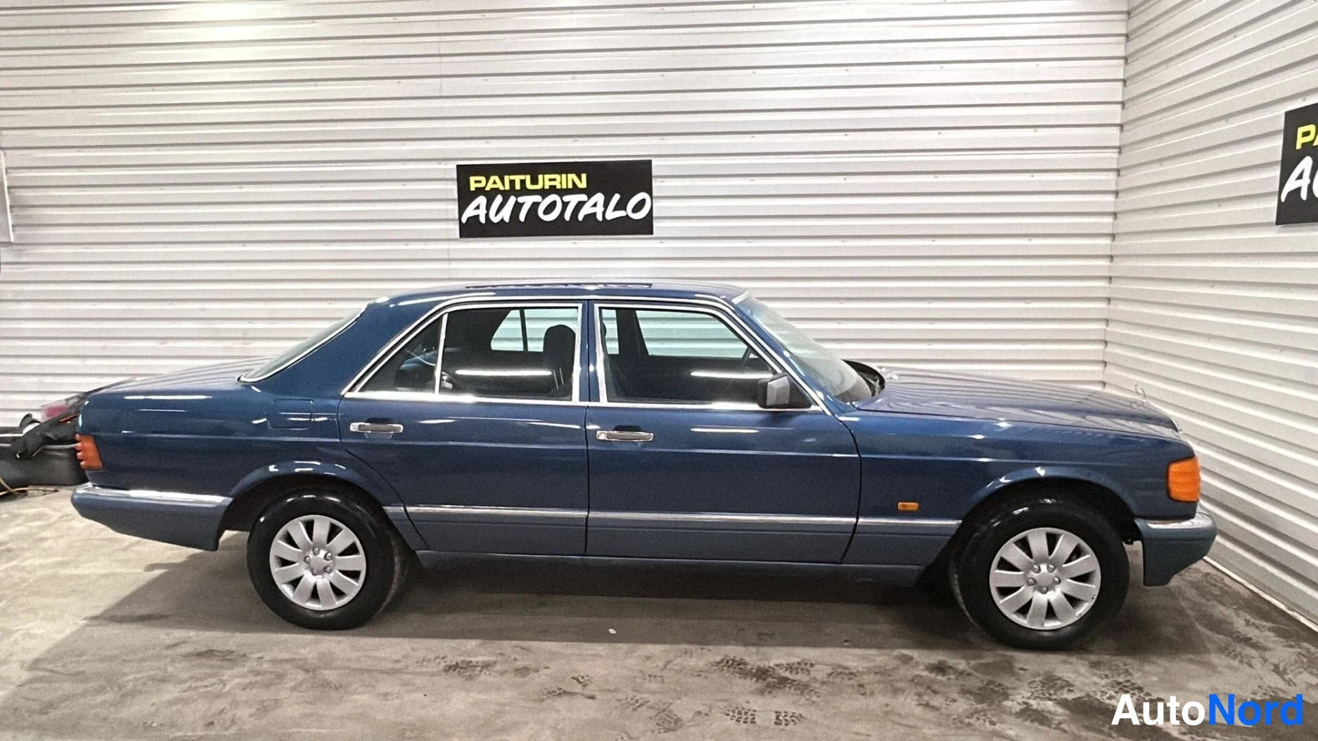 Sivulta: Sininen Mercedes-sedan täysin sivulta vasemmalle katsottuna sisätiloissa.