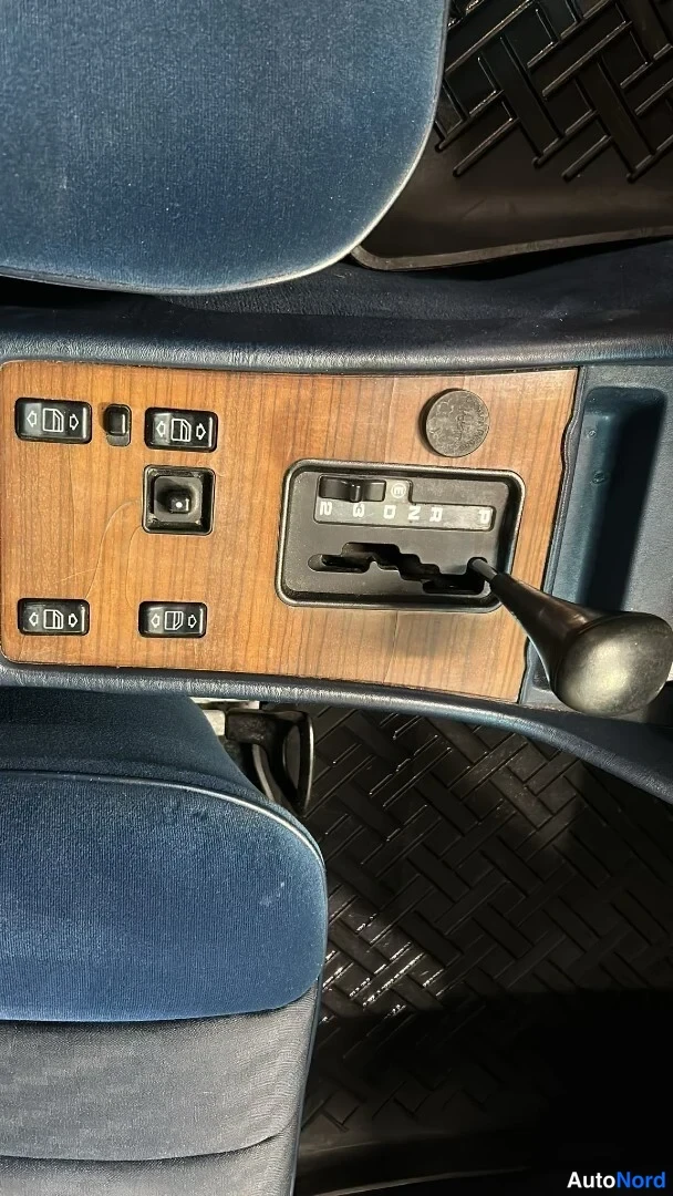 Edestä: Keskikonsolin puukoristeinen paneeli sähköikkunan napeilla ja automaattivaihteen valitsimella, merkinnät P R N D 3 2