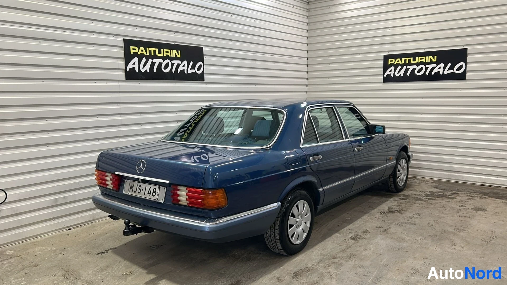 Takaviisto: Sininen Mercedes-sedan takakulmakuva vasemmalta; rekisterikilpi ja takaosa näkyvät vasemman sivuongelman kanssa.