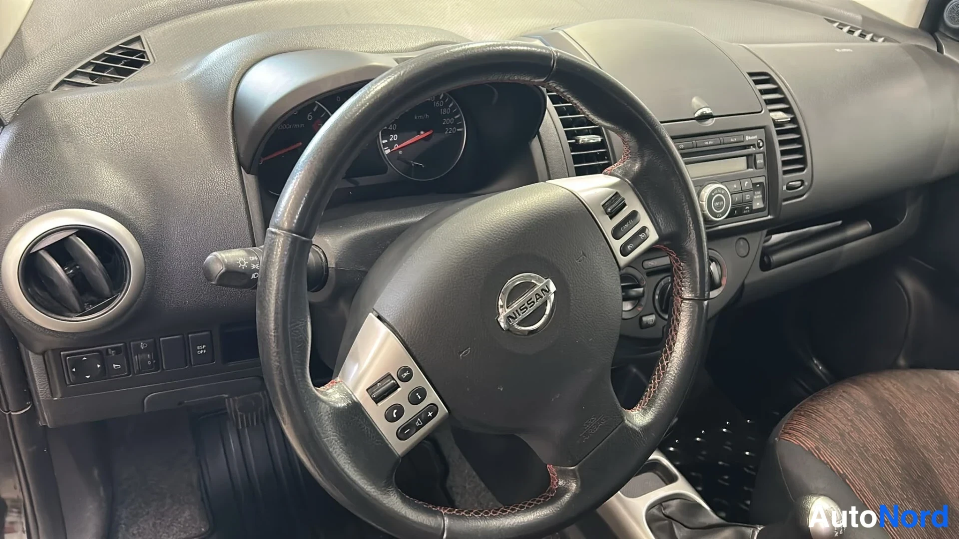 Muu: Nissan Noten ohjaamopaikka: Nissan-merkitty monitoimiratti, mittaristo ja radiotaajuuksien radioyksikkö kojelaudassa.