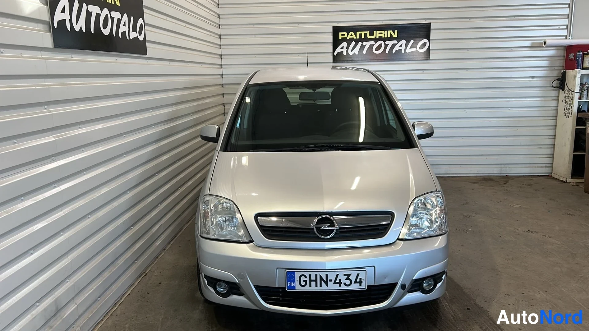 Edestä: Hopeanvärinen Opel Meriva suoraan edestäpäin sisätiloissa, rekisteritunnus.