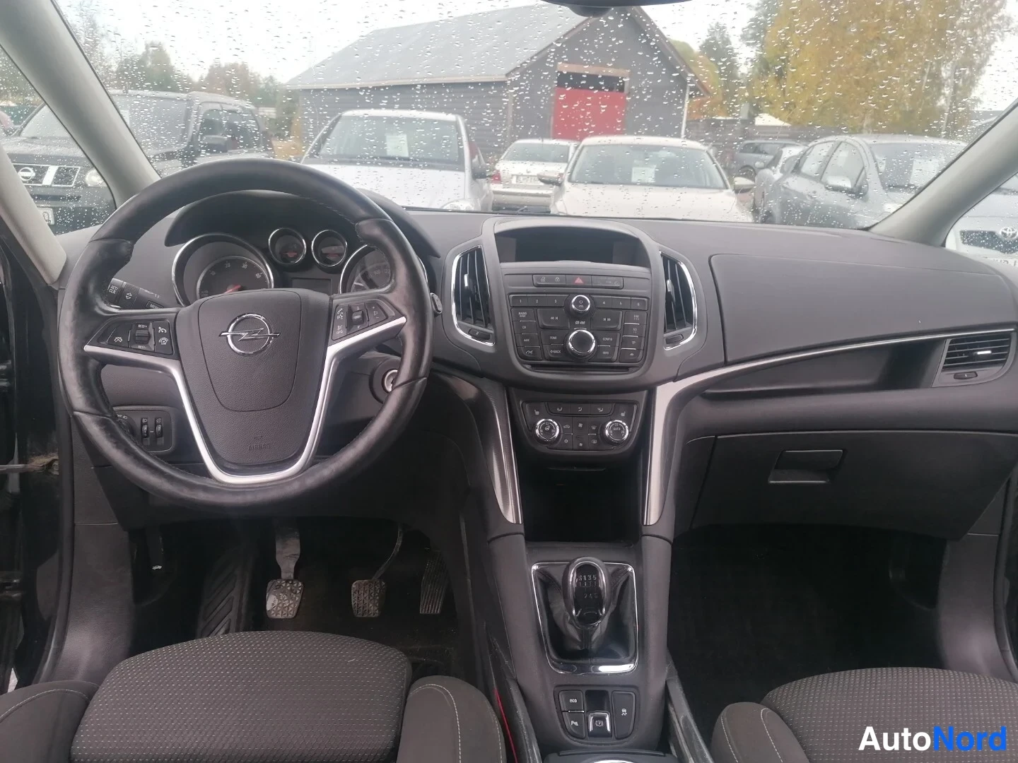 Ohjaamo: Front cabin interior view of a steering wheel with controls, instrument cluster, central infotainment screen, gear selector, and front seats.