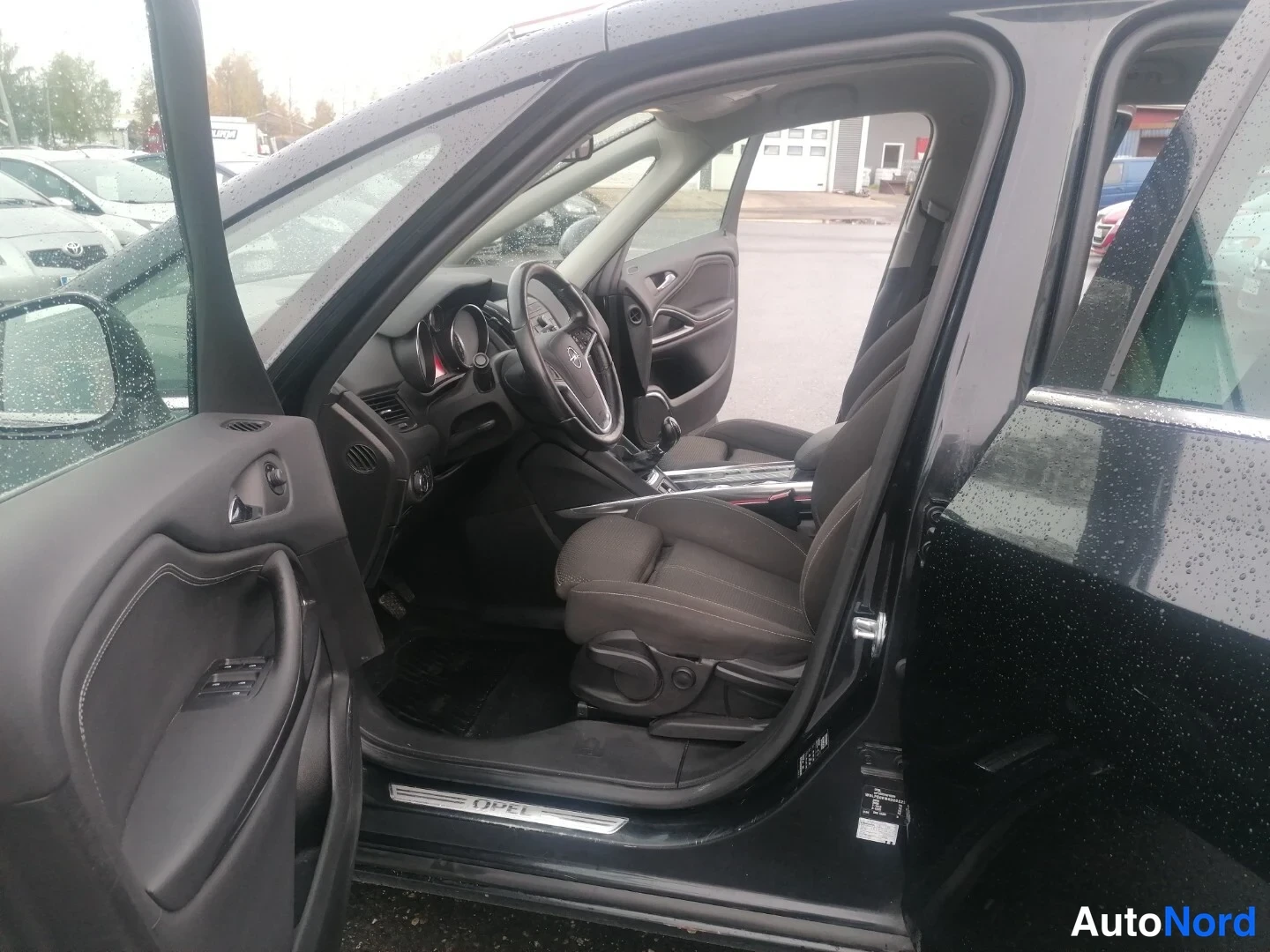 Etuistuimet: Interior of the driver seat with the driver door open; dashboard and steering wheel visible.