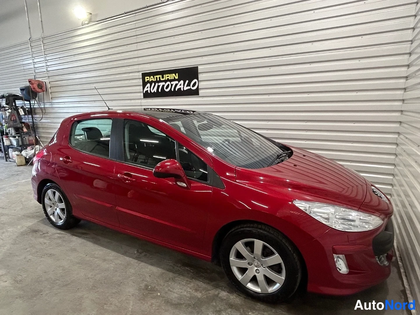 Etuviisto, nokka oikealle: Punainen Peugeot 308 -henkilöauto kuvattu etukulmasta oikealta autotallin sisätiloissa.