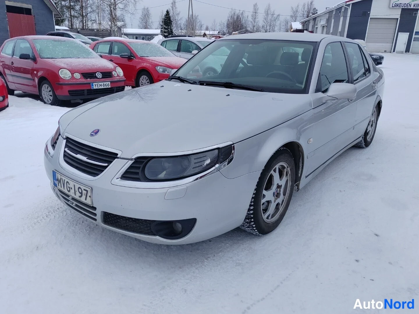 Etuviisto, nokka vasemmalle: Saab-henkilöauto edestä vasemmalta kolmeneljännesnäkymässä lumisella pihalla, hopeanvärinen korimalli.