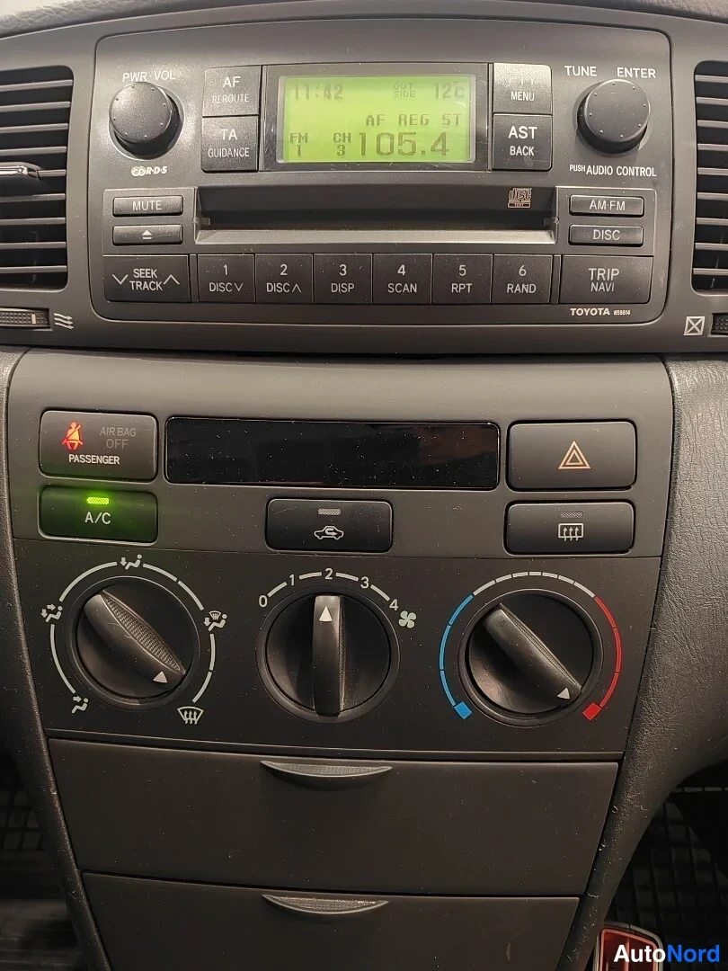 Yksityiskohta: Toyota Corollan kojelauta: Toyota-radio, jossa näkyy FM 105.4 ja kello 11.42, sekä A/C-painike, joka on valaistu vihreällä.