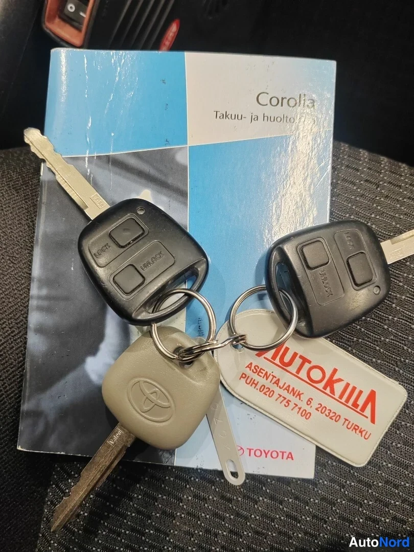Yksityiskohta: Toyota Corollan sinivalkoinen Takuu- ja huoltokirja sekä kaksi avainkaukosäädintä ja Toyota-avain renkaalla, jossa AutoKiila-nimike.