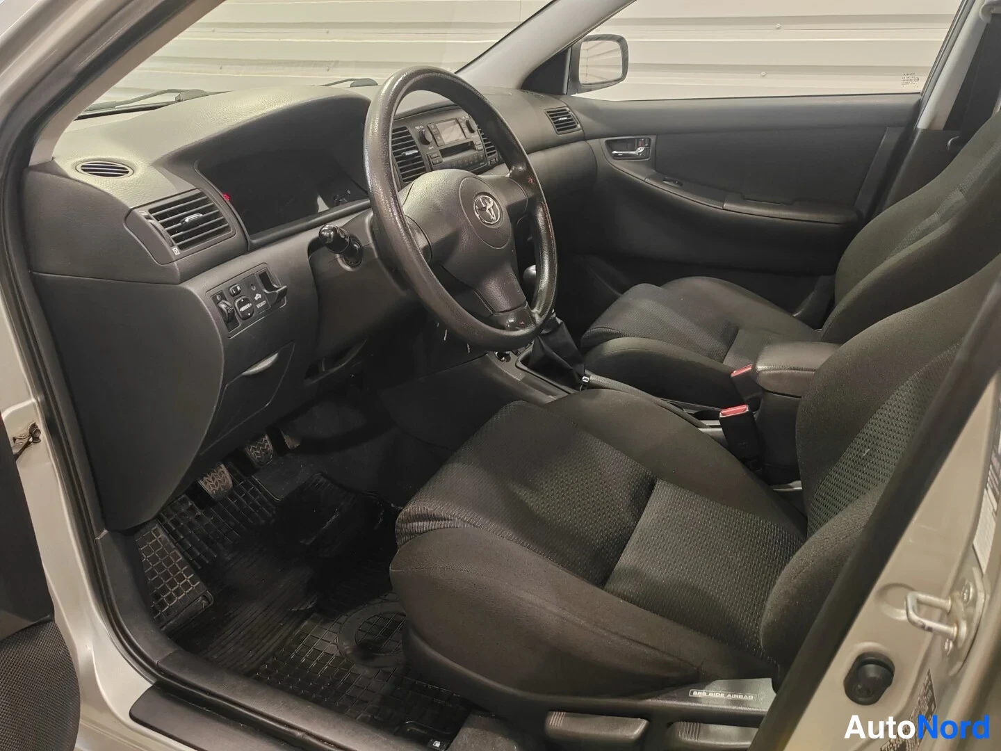 Edestä: Toyota Corolla -auton sisätilat: ratin ja kojelaudan näkymä kuljettajan puolelta.