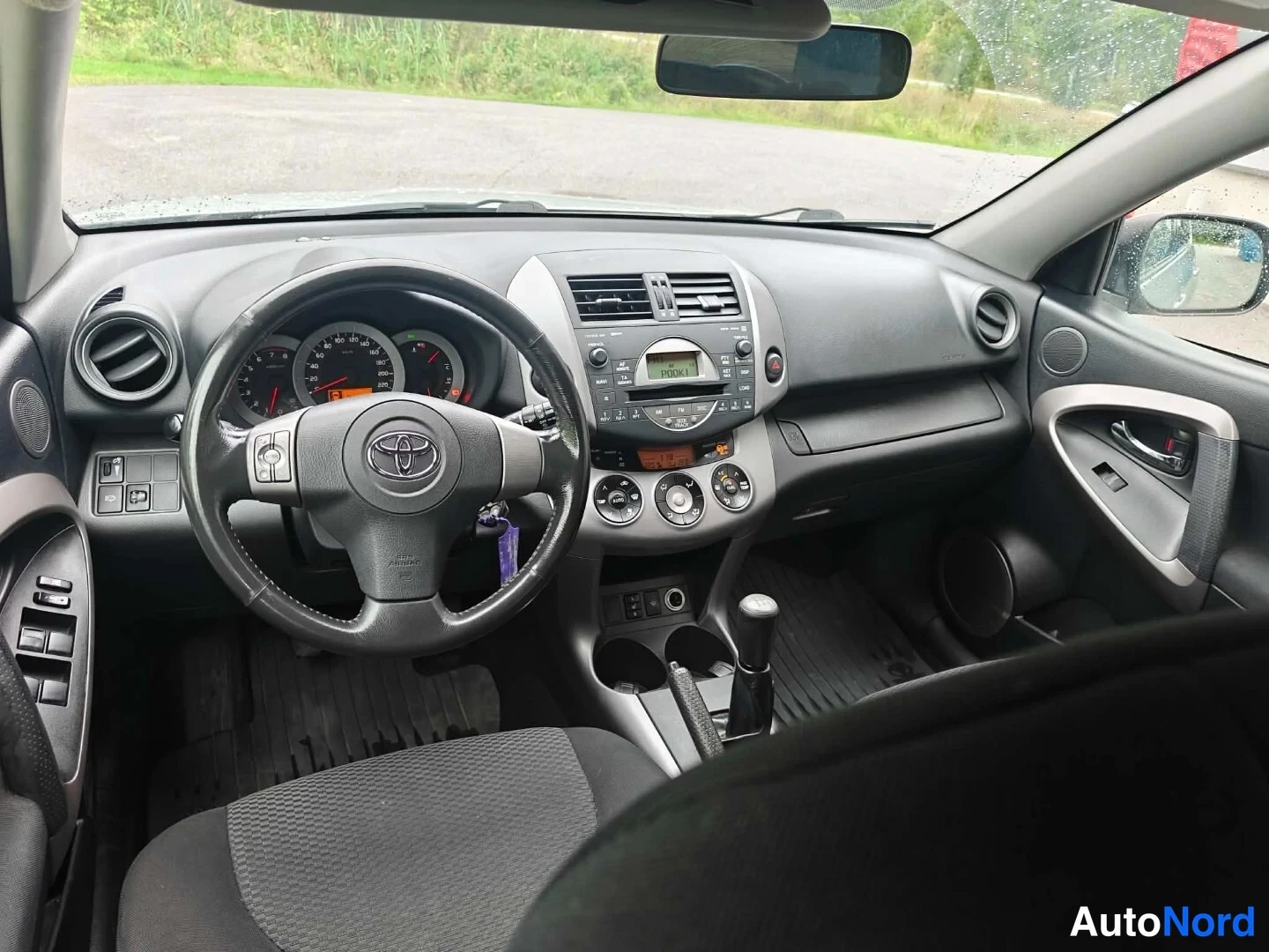 Muu: Auton sisätilat etupenkiltä kuvattuna: Toyota-ohjauspyörä, mittaristo, manuaalivaihtean vtkahva ja keskikonsoli.