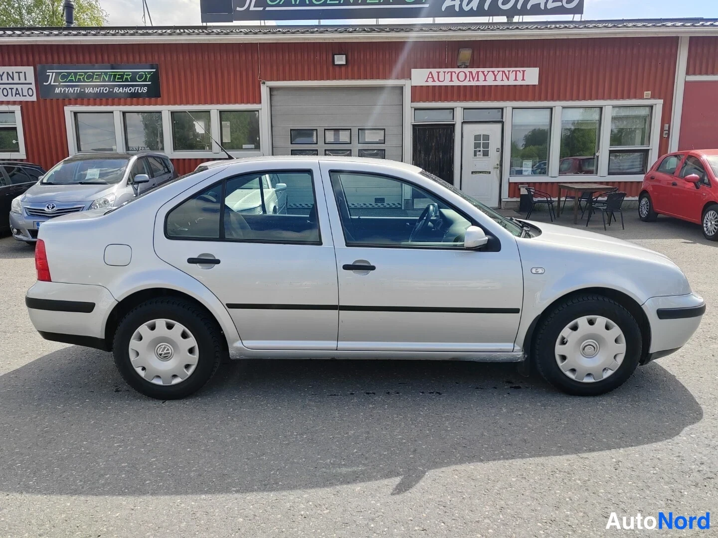 Sivulta: Hopeanharmaan Volkswagen Bora -sedanin sivuprofiili, oikea kylki kuvattuna autotallin edessä.