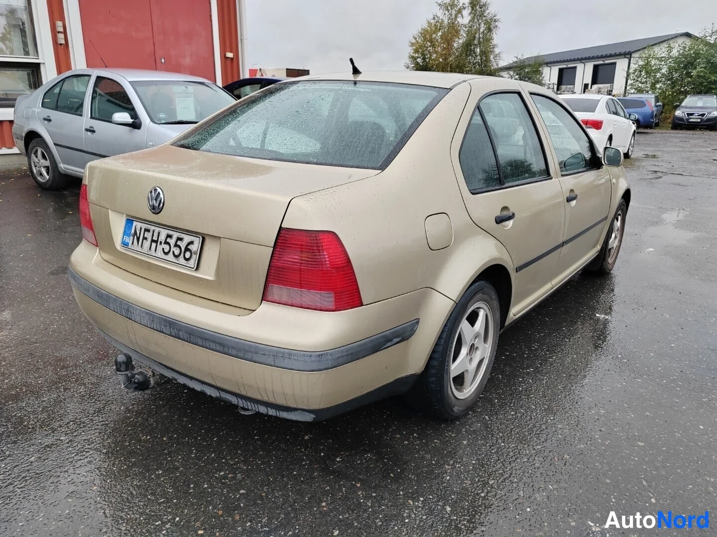 Takaviisto: Kultaisen Volkswagen Bora -sedanin takakulma vasemmalta, rekisterikilpi, päällirakennus takapuskurissa.