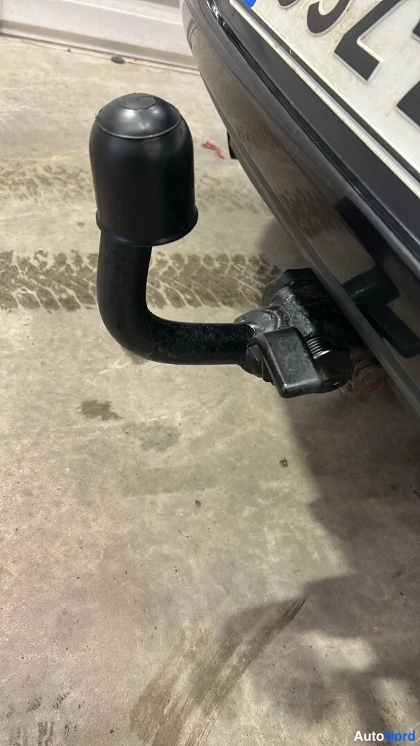 Yksityiskohta: Mustan auton takaosaan kiinnitetty irrotettava vetokoukun kaula pölyisellä betonilattialla.