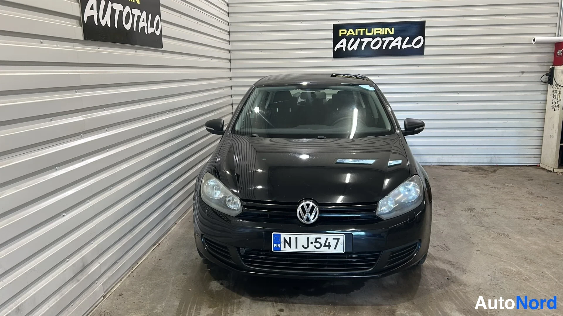 Edestä: Mustan Volkswagen Golf -viistoperän suora etukuva hallissa.