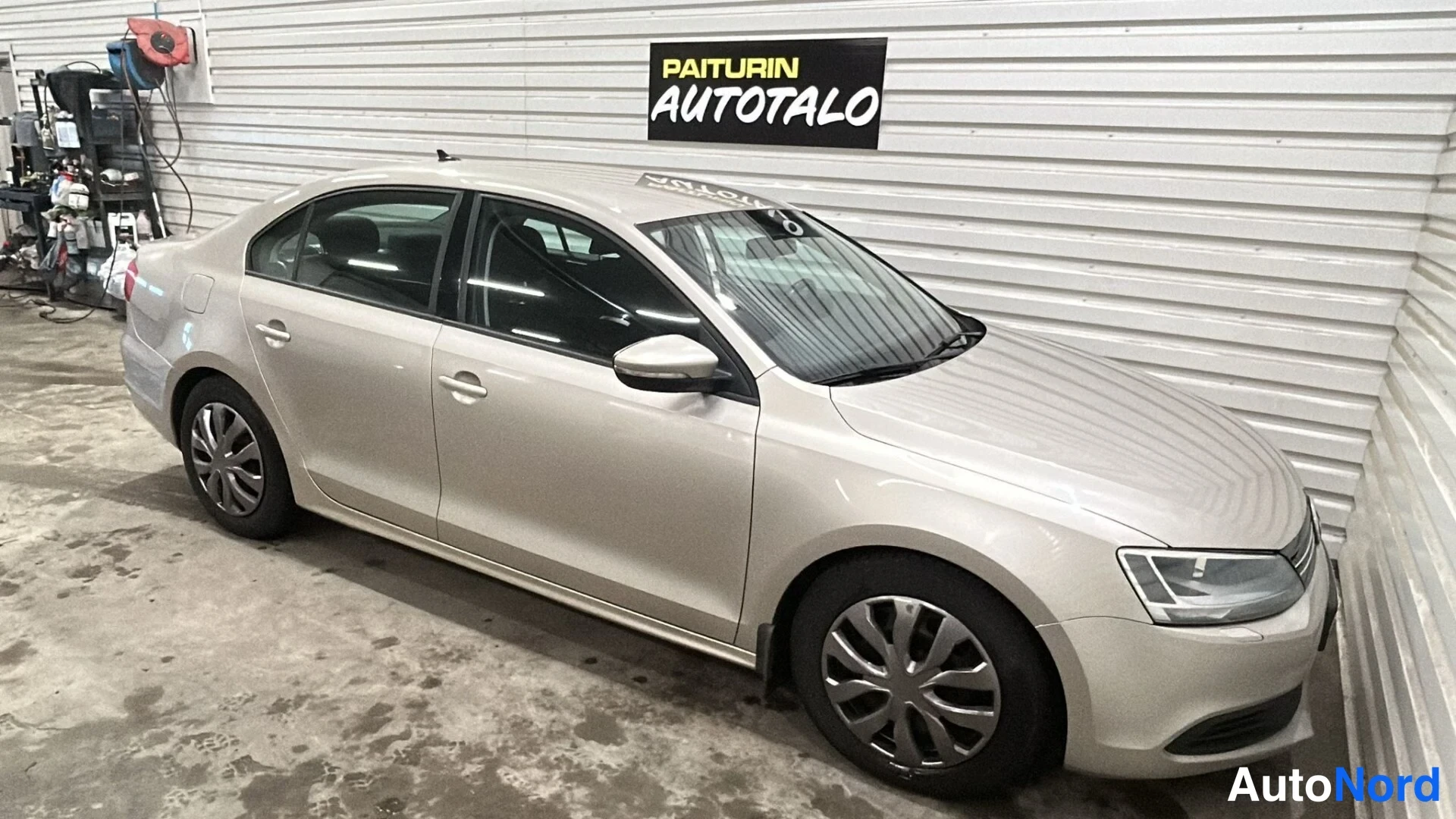 Etuviisto, nokka oikealle: Volkswagen Jetta -sedanin etukulman vasemmalta; beige-kultainen kori, etusuoja, etupyörä ja kylki näkyvät varastotilassa.