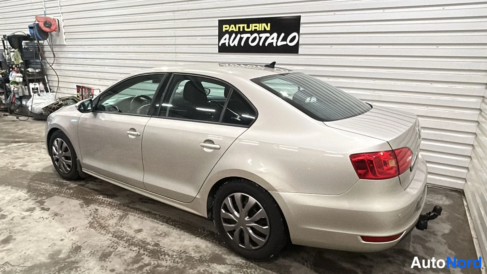 Takaviisto: Volkswagen Jetta -henkilöautin takaosalinäkymä sisätiloissa, vaaleanbeige koriväri, takavalo ja perävaunukoukku näkyvissä.