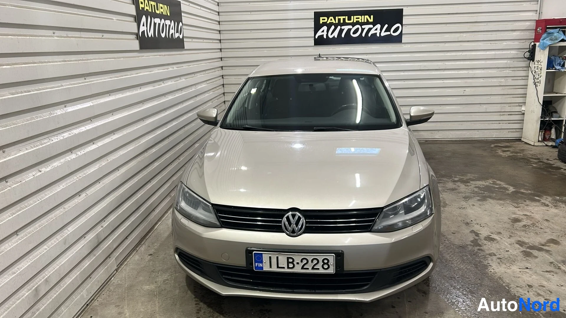Edestä: Volkswagen Jetta etupäin hallissa, vaaleanbeige korivalo ja rekisterikilpi.