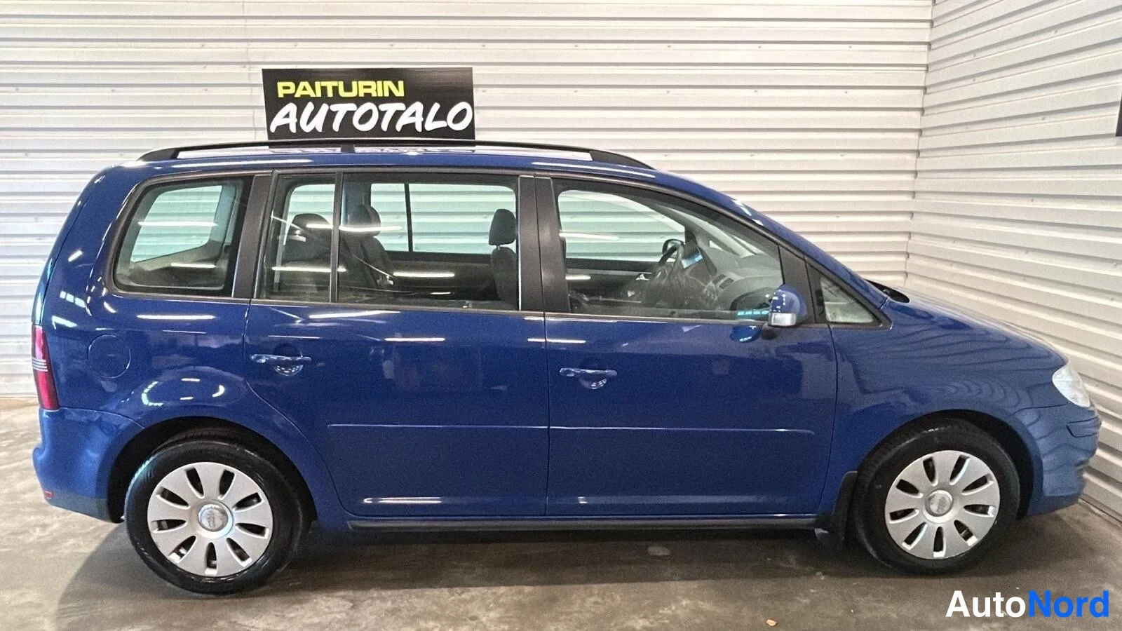 Etuviisto, nokka oikealle: Sininen farmarimappeauto sisätiloissa kylkiviistosta, keula oikeassa reunassa.