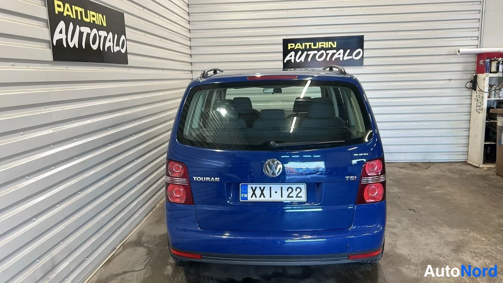 Takaa: Sininen Volkswagen Touran suoraan takaa kuvattuna sisätilassa, rekisterikilpi.