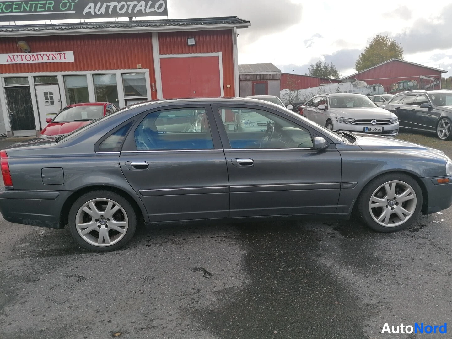 Etuviisto, nokka oikealle: Sivukulmakuva tummanharmaasta Volvo S80 -sedanista autotallin pihalla, koko kylki ja etuosa osittain näkyvissä.