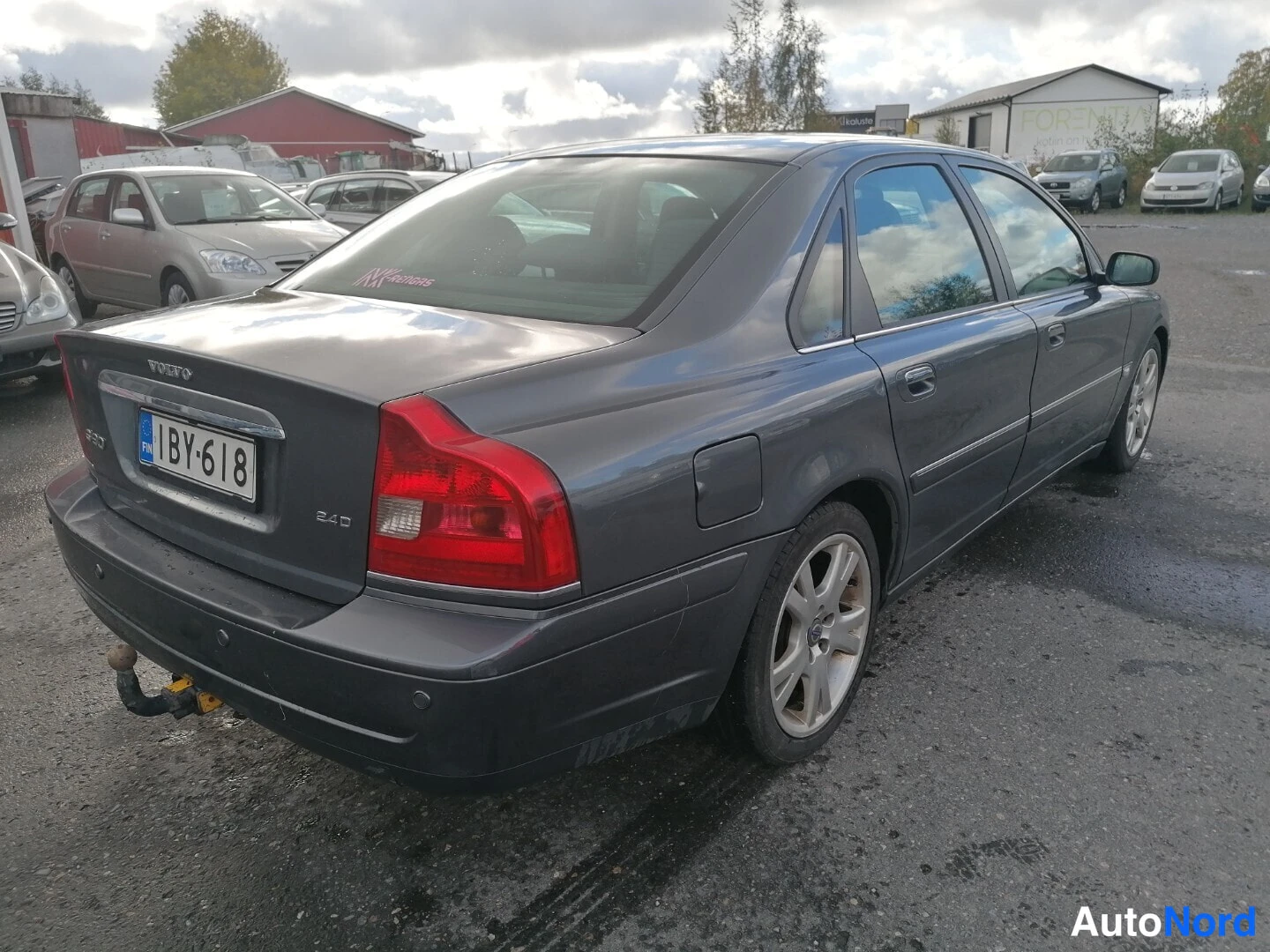 Takaviisto: Takakolmanneskulma tummanharmaasta Volvo S80 -sedanista; VOLVO-merkki, rekisterikilpi ja vetokoulu näkyvissä.