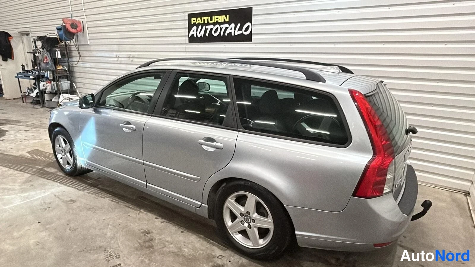 Takaviisto: Hopeanharmaa farmariauto sivulta takaa kuvattuna autotallissa, katto screillä.