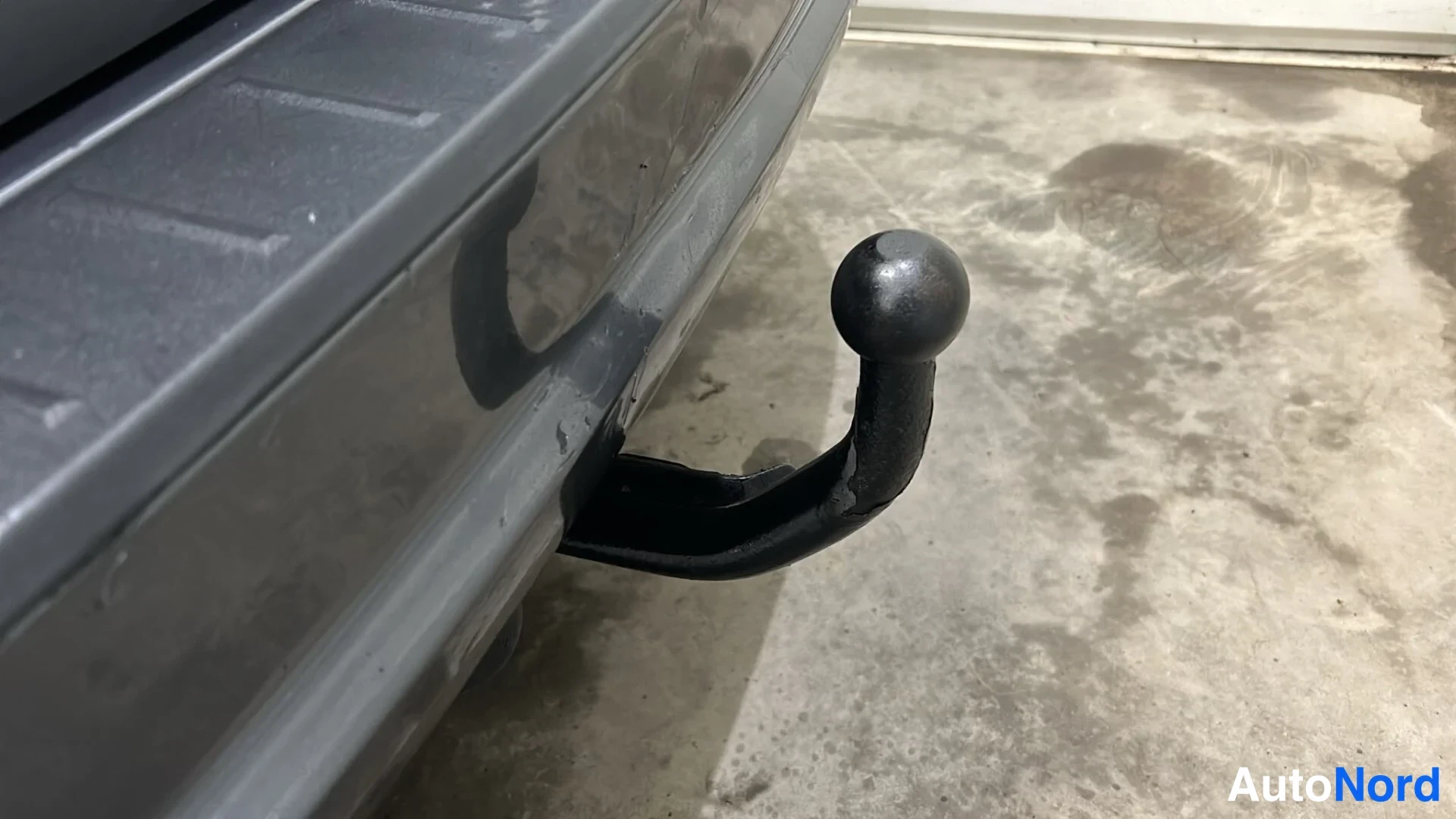 Takaa: Kiinteä vetokoukun kytkinpallo auton takapuskurin alla betonilattiaa vasten.