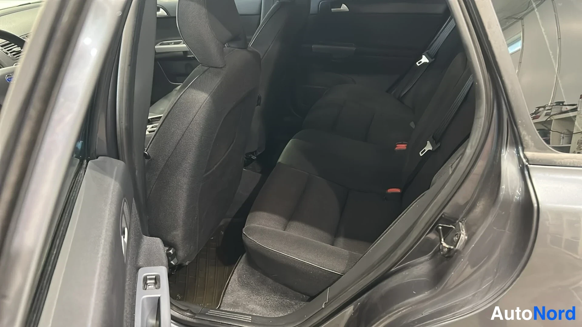 Muu: Volvo V50:n takaistuin avoimesta takaovesta katsottuna; tummat kangasistuimet ja turvavyöt.