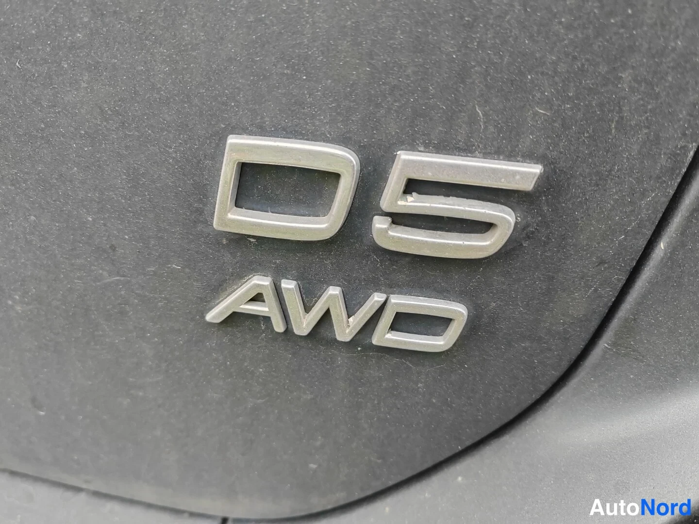 Muu: Metallinen merkintä D5 AWD auton takaosassa, pölyinen pinta.
