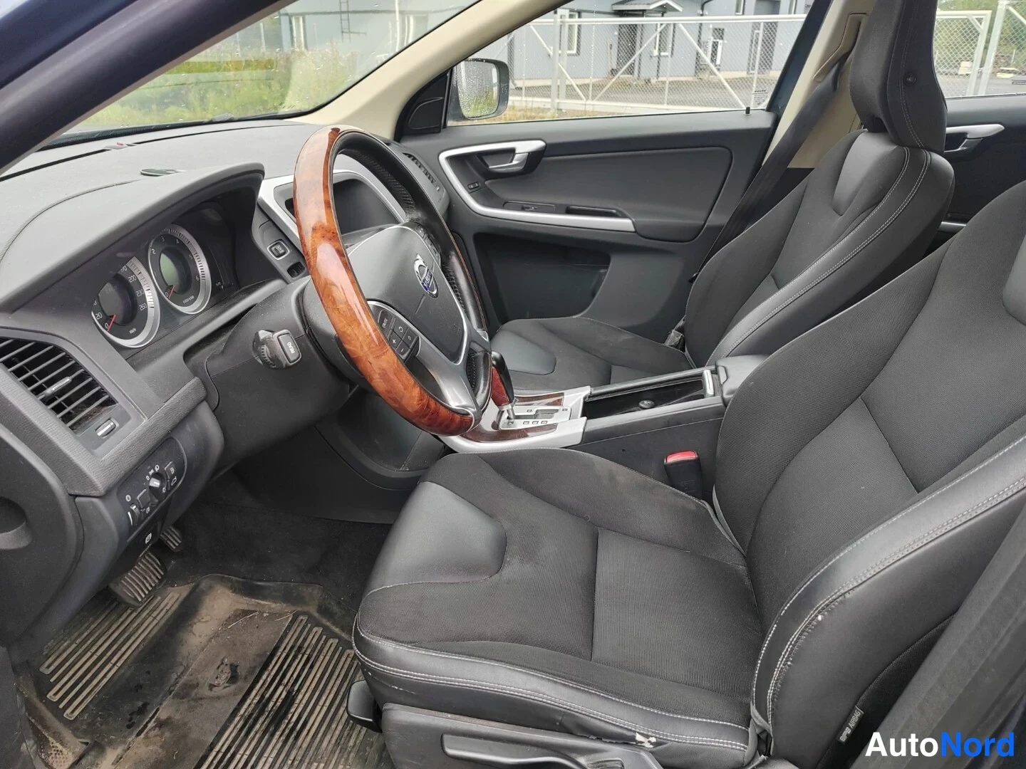 Muu: Auton sisätilat: Volvo-ohjauspyörä puukiiltoreunuksella, tummat kangasistuimet ja tumma kojelauta.