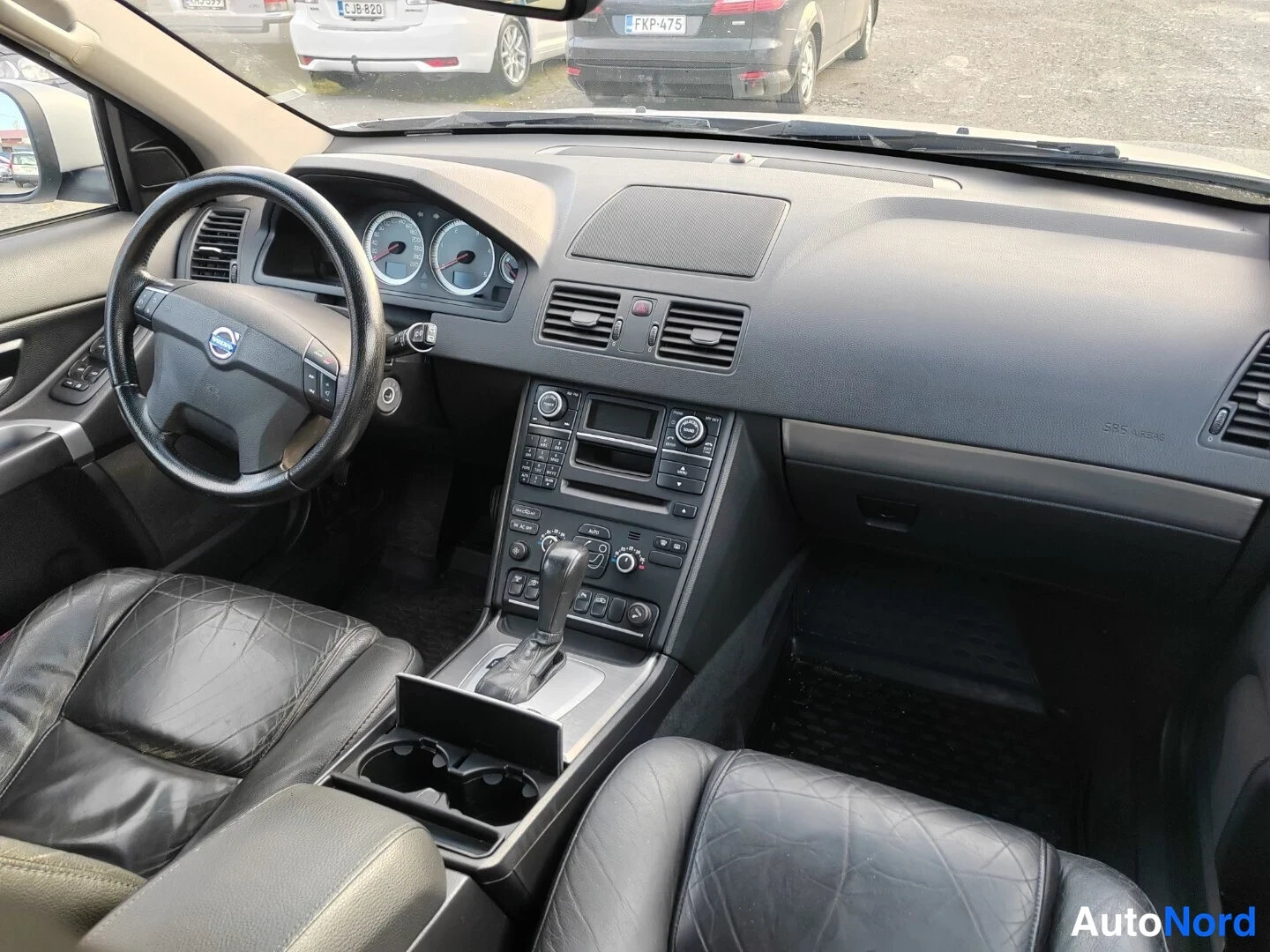 Muu: Volvo XC90:n ohjaamo etumatkalta: Volvon logollinen ohjauspyörä, mittaristo, radio- ja ilmastointilaitteet keskikonsolissa sekä automaattivaihteen valitsin.