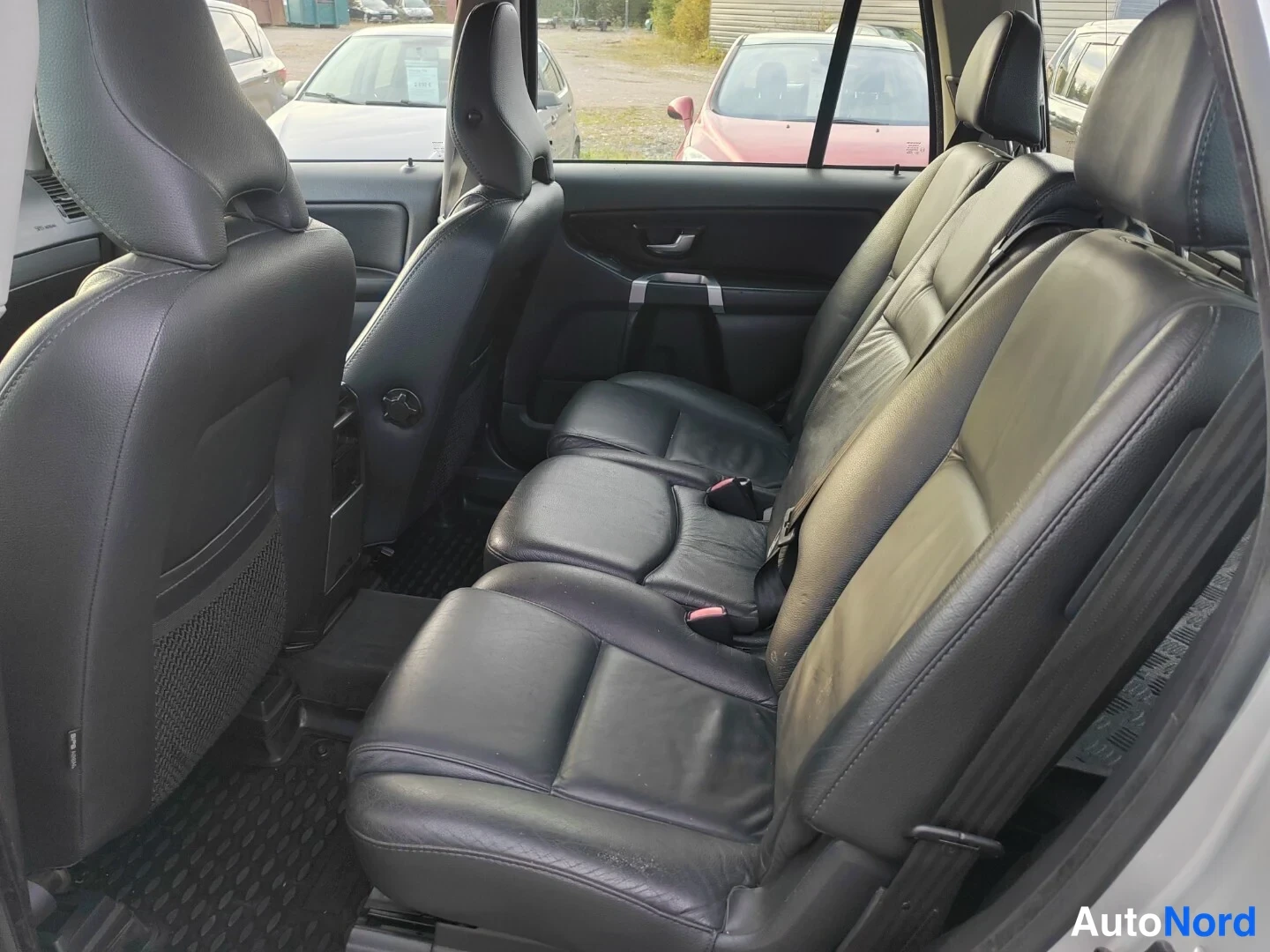 Muu: Volvo XC90:n takapenkkialue takaa päin kuvattuna: mustat nahkaistuimet, avattu takariovi ja matotilan kumimatto.