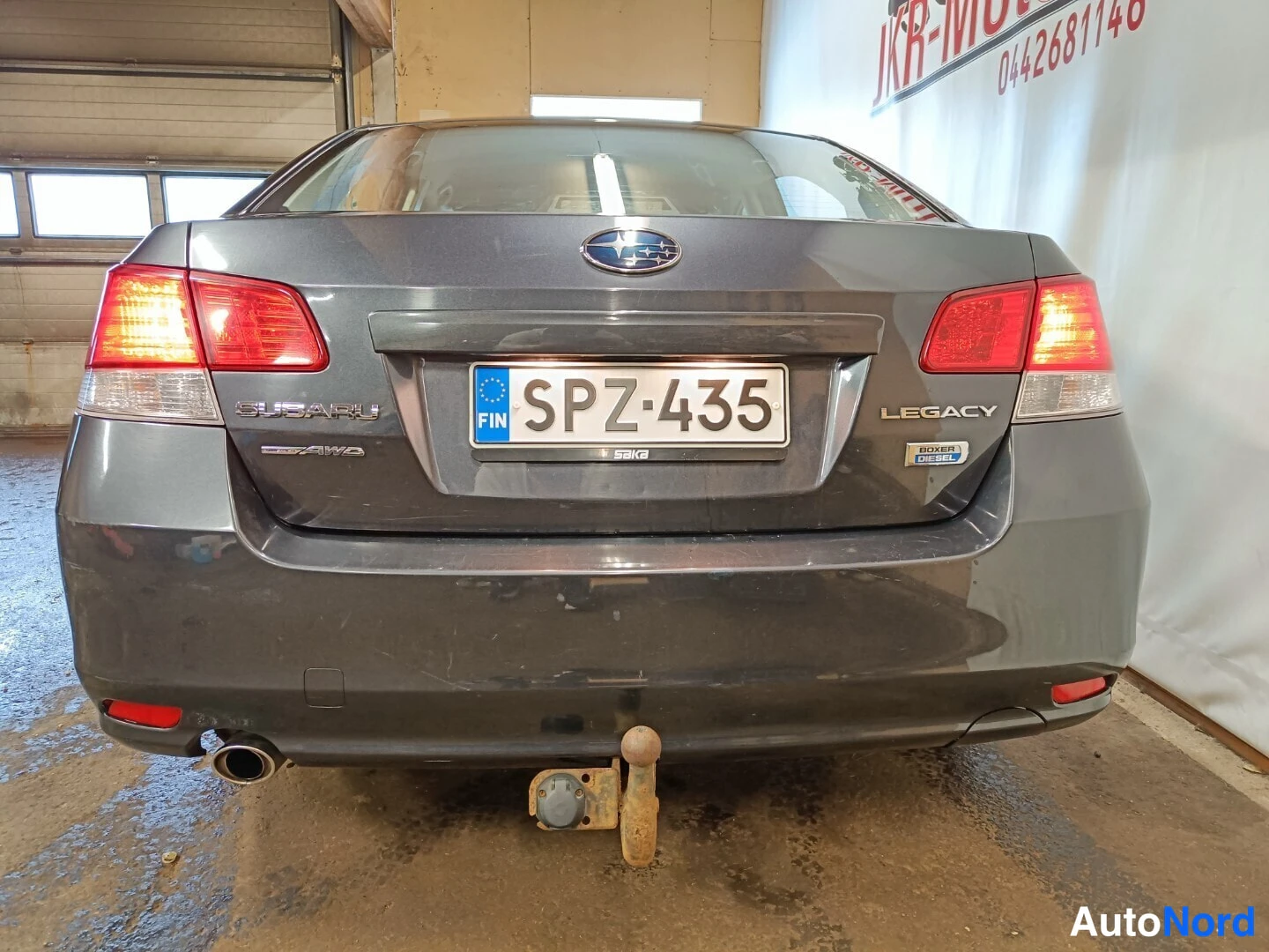 Takaa: Tummanharmaan sedanin takaosa suoraan; rekisteritunnus, SUBARU- ja LEGACY-merkinnät sekä peräkoukku.