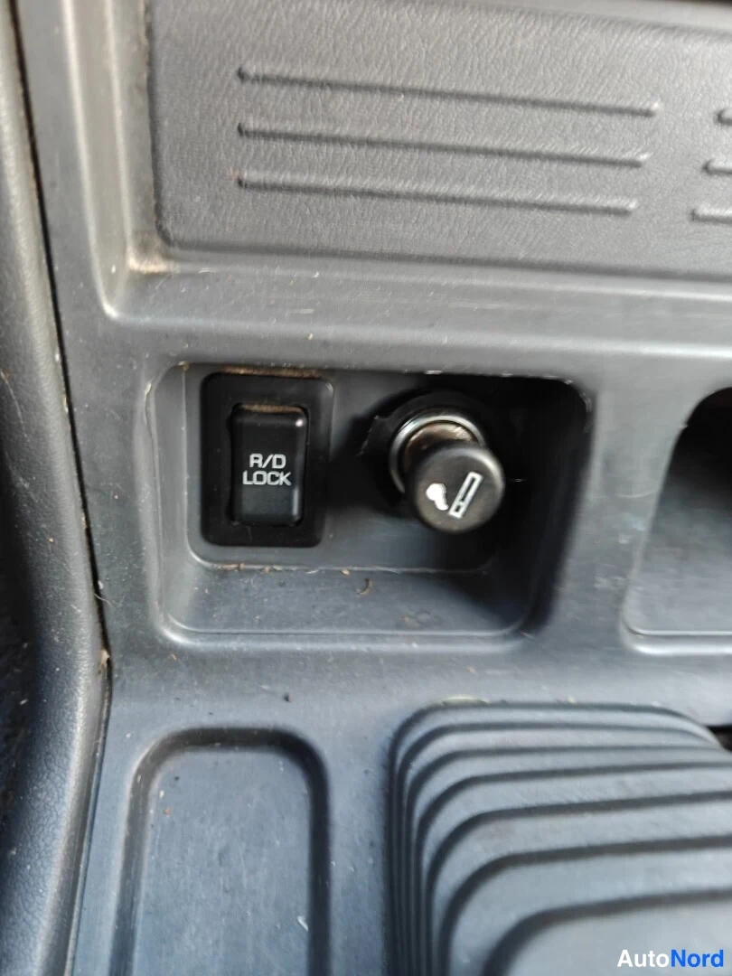 Muu: Lähikuva keskikonsolissa olevasta R/D LOCK -kytkimestä ja sen vieressä olevasta pyörävaihtajanupista.