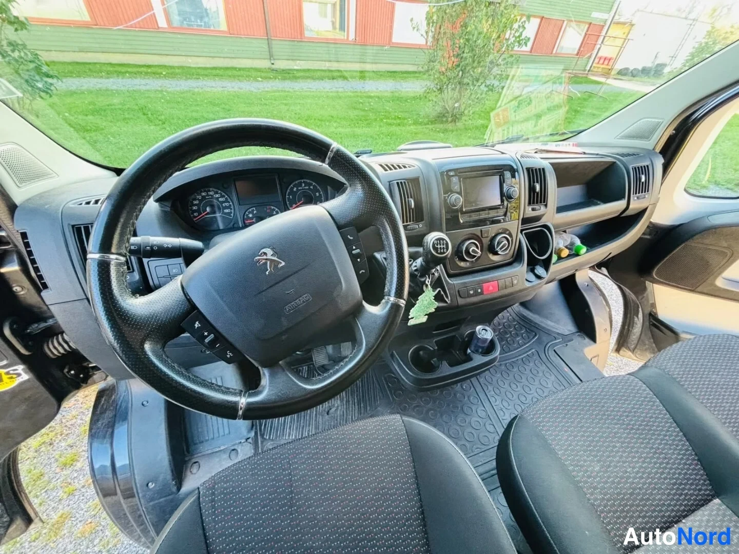Muu: Peugeot-ohjaamo ylhäältä: ohjauspyörä Peugeot-emblemillä, kojelaudan mittarit, radio ja manuaalivaihteiston vaihdekeppi.