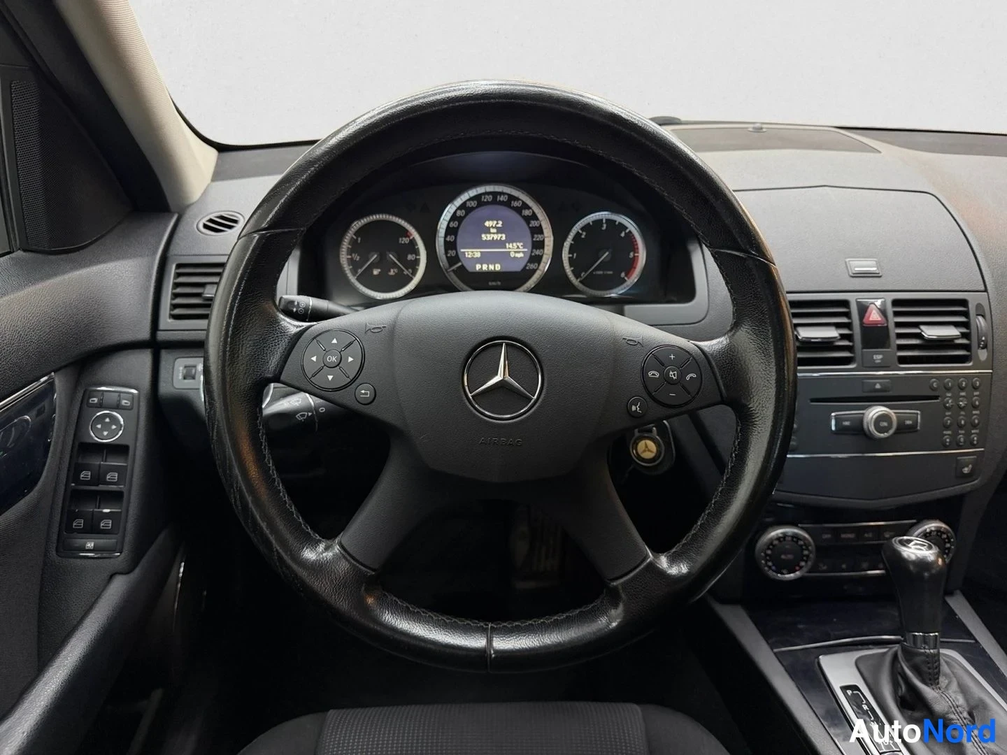 Edestä: Mercedes-tunnuksellinen ohjauspyörä, mittaristo ja keskikonsoli, vaihteenvalitsin P-asennossa.