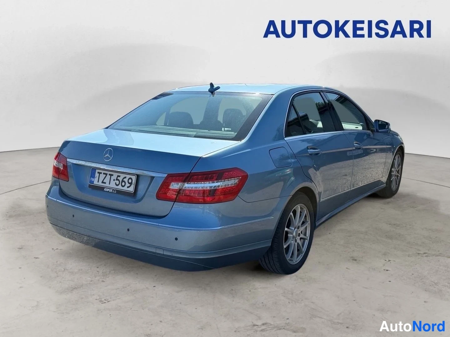 Takaviisto: Sininen Mercedes-Benz E-sarjan sedan kuvattu takaa kolmanneltasektoralta vasemmalta, perä ja kylki näkyvissä studiossa.