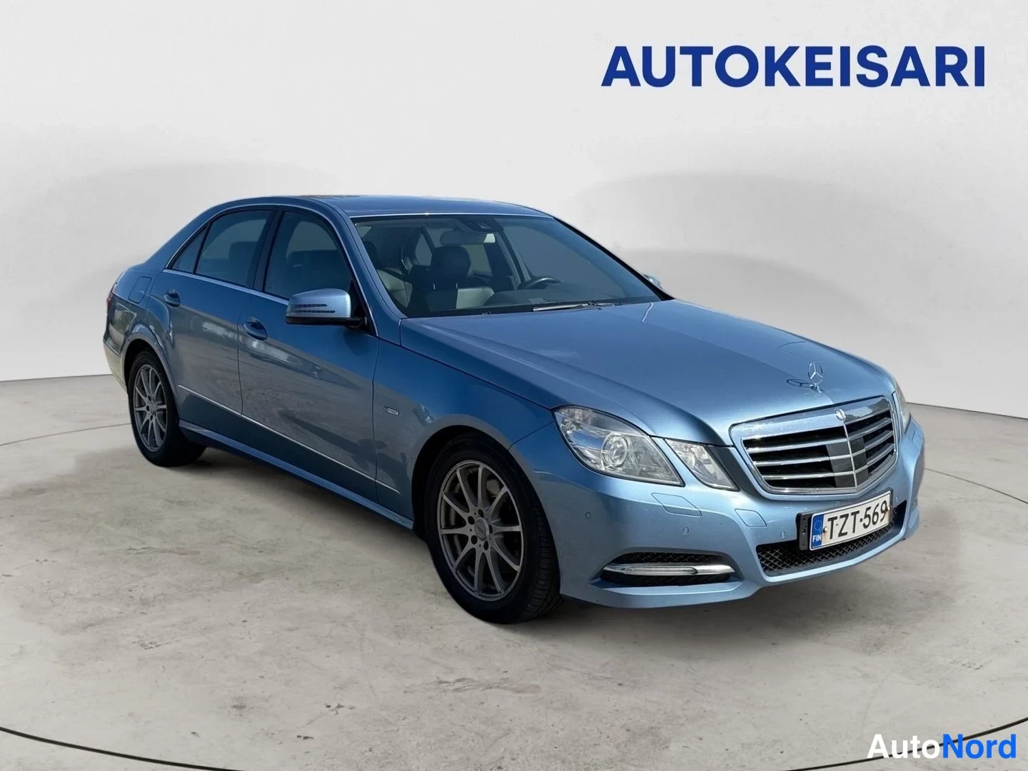 Etuviisto, nokka oikealle: Sininen Mercedes-Benz sedaaninen etuviistöstä oikealta, keulakilpi ja rekisterikilpi näkyvät.