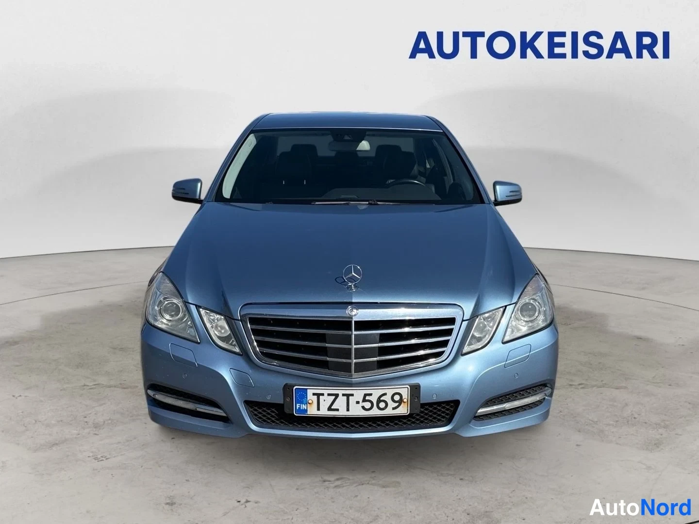 Edestä: Sininen Mercedes-Benz edestäpäin, etusäleikkö, ajovalot ja rekisterikilpi näkyvät.