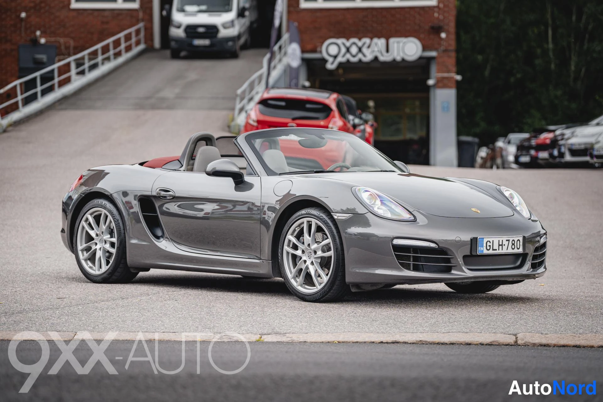 Etuviisto, nokka oikealle: Porsche Boxster avomalli kuvattu etu kolmasosan kuvakulmasta, keula oikealla; autossa harmaa koria ja avattu katto, rekisterissä.