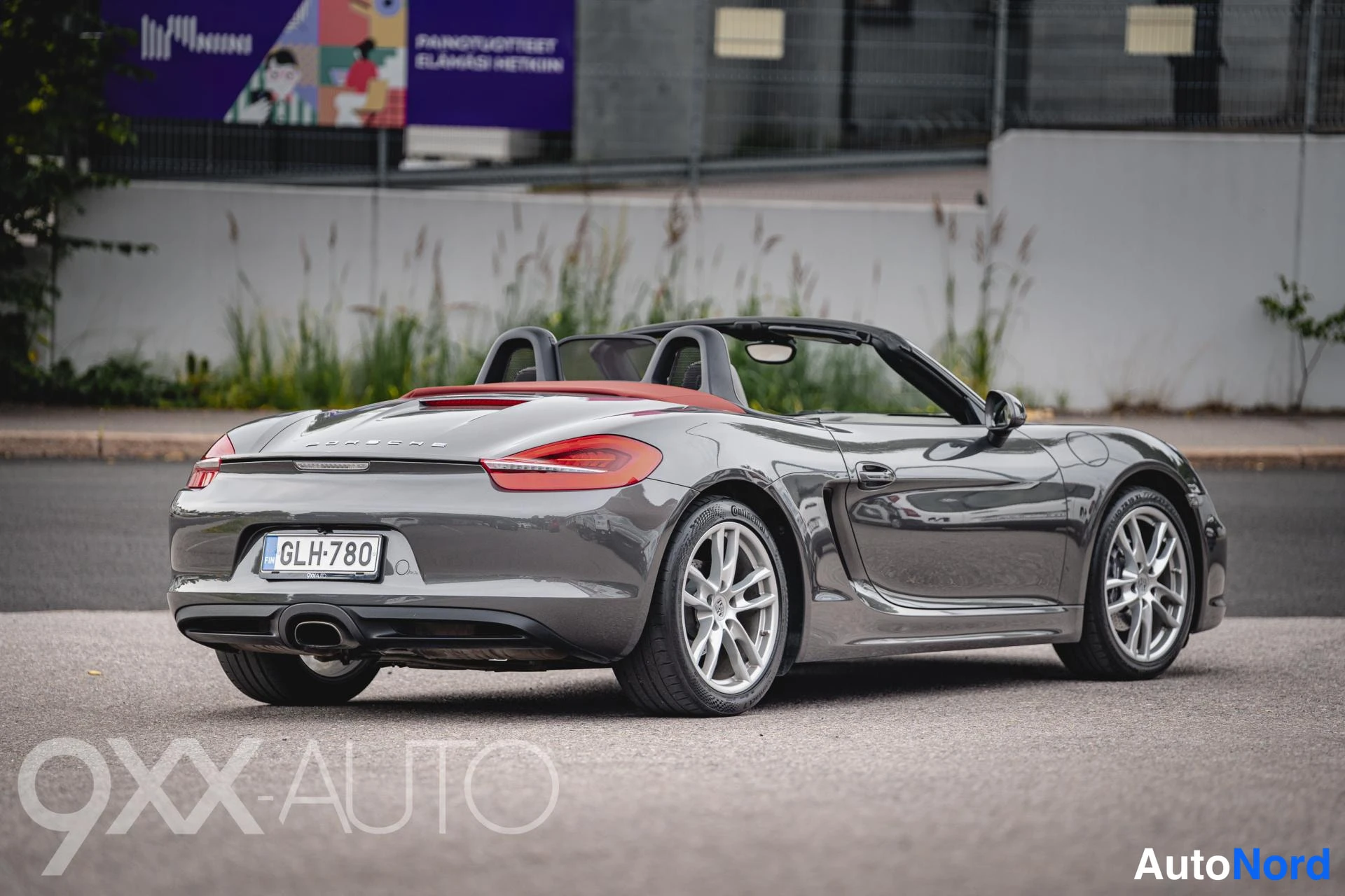 Takaviisto: Porsche Boxster-avoneva takaa oikeasta kulmasta kuvattuna, katto auki, punainen kansi, takavalot ja rekisteri näkyvissä.