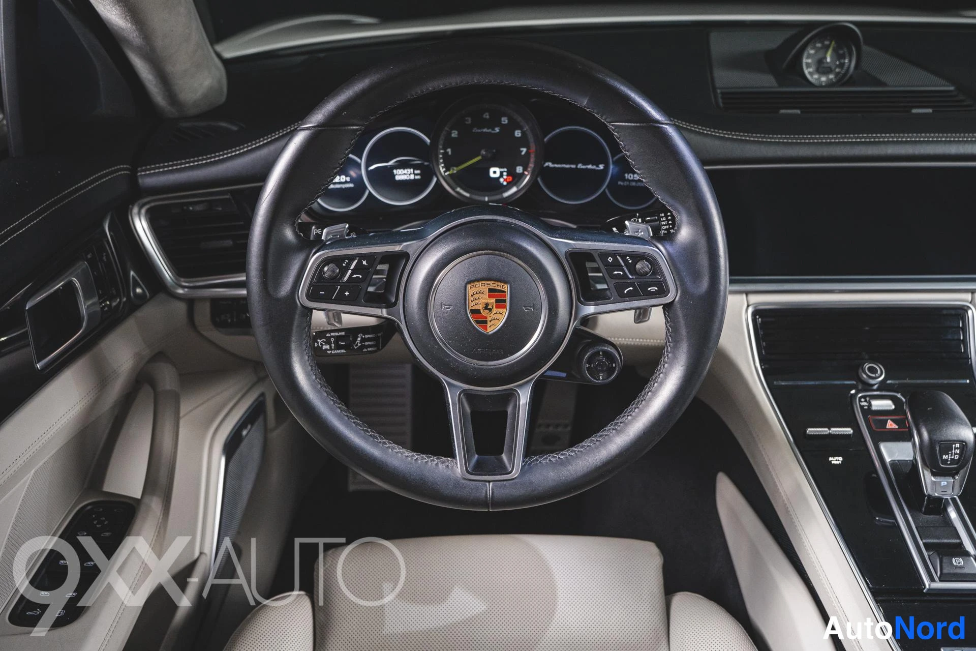 Etuviisto, nokka oikealle: Ohjauspyörä ja mittaristo lähikuvassa: Porsche-logollinen ohjauspyörä, analoginen keskimittari ja infotainment-näytön reuna.